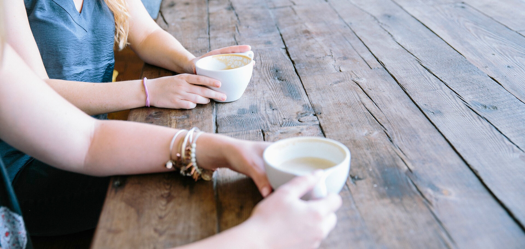 Life coach speaking with client over coffee at rustic table.